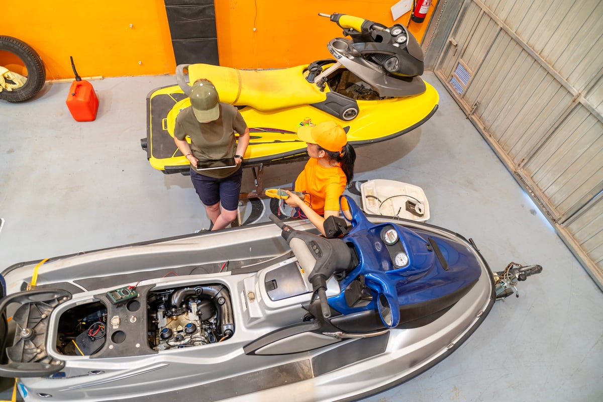 Mechanics using a tablet and multimeter to diagnose a personal watercraft engine